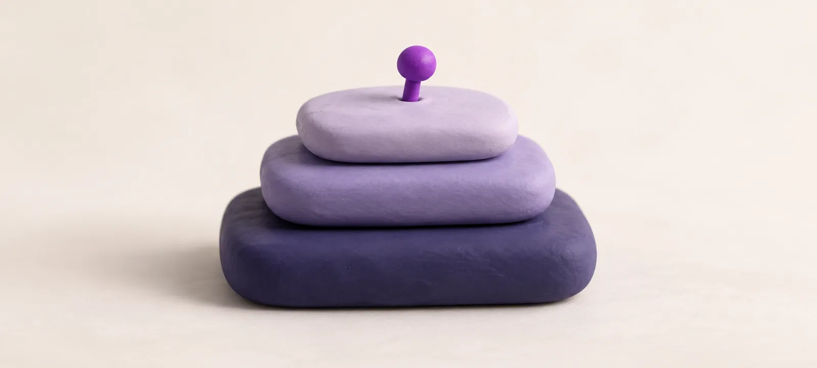 A neat stack of smooth clay tablets, each smaller than the one below, with a small violet pin pressed into the top one