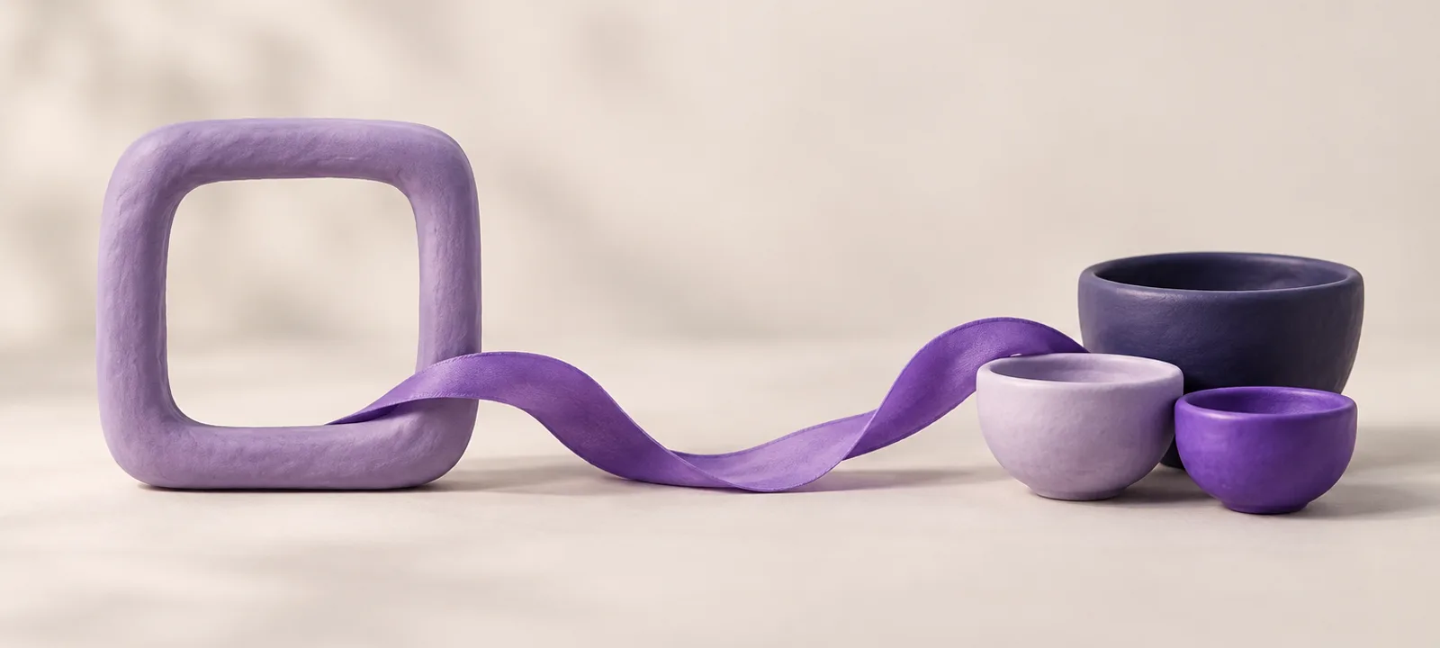 A rounded square clay frame on the left with a thin ribbon flowing from it across the surface to a cluster of small round clay bowls